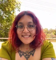 Achi Vasquez smiling outdoors, red hair and glasses